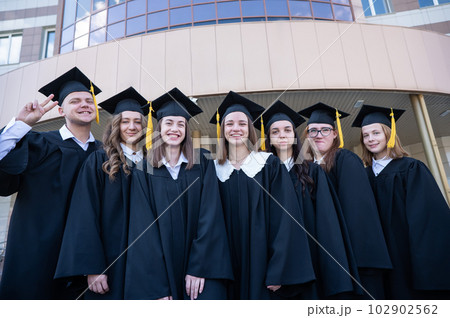 Happy students in graduate gown stand in a row against the backdrop of the university. Happy students in graduate gown stand in a row against the backdrop of the university. 102902562