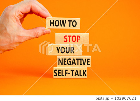 Stop negative self-talk symbol. Concept words How to stop your negative self-talk on wooden block. Psychologist hand. Beautiful orange background. Psychological negative self-talk concept. Copy space 102907621