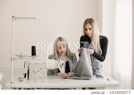Two young seamstresses sitting on the sewing machine in her workshop 102908077