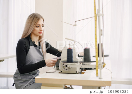 Young seamstress sitting on the sewing machine in her workshop 102908083