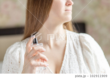 Beautiful young woman with bottle of perfume at home, closeup Beautiful young woman with bottle of perfume at home, closeup 102911909