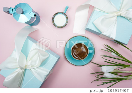 A cup of coffee and a gift box with a white bow on a pink background. 102917407