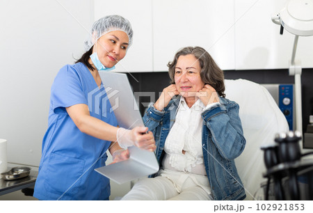 Satisfied elderly woman patient looks in the mirror after the procedure Satisfied elderly woman patient looks in the mirror after the procedure 102921853