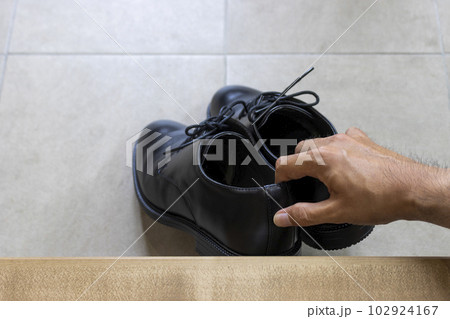 玄関でビジネスシューズを持ち上げる男性の手 102924167