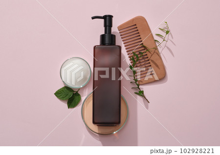 Scene for advertising products - amber bottle container shampoo with comb, petri dishes filled foam and green leaf on pink background. Mockup for design, organic cosmetics, beauty products concept Scene for advertising products - amber bottle container shampoo with comb, petri dishes filled foam and green leaf on pink background. Mockup for design, organic cosmetics, beauty products concept 102928221
