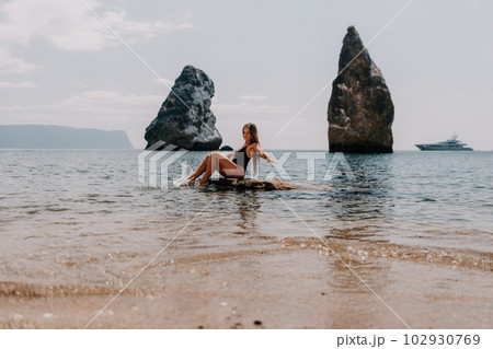 Woman summer travel sea. Happy tourist enjoy taking picture outdoors for memories. Woman traveler posing on the beach at sea surrounded by volcanic mountains, sharing travel adventure journey Woman summer travel sea. Happy tourist enjoy taking picture outdoors for memories. Woman traveler posing on the beach at sea surrounded by volcanic mountains, sharing travel adventure journey 102930769
