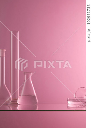 Several laboratory glassware containing transparent liquid are placed on a glass table with purple background. Blank space to display product 102931738