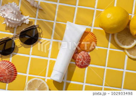 Flat lay of an unbranded cosmetic container decorated with Lemons, a sunglasses and colorful seashells. Lemon (Citrus limon) is a natural method of increasing collagen in facial skin Flat lay of an unbranded cosmetic container decorated with Lemons, a sunglasses and colorful seashells. Lemon (Citrus limon) is a natural method of increasing collagen in facial skin 102933498