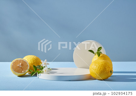 Blue background with fresh lemons, white flower and round podium. Blank space for display product of lemon ingredient. Lemon has many good uses for health and beauty. 102934175