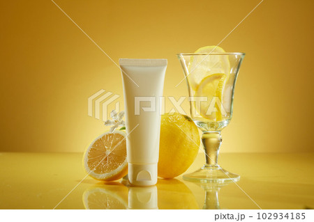 Simple but classy concept for cosmetic advertisement with lemon extract. Plastic tube unlabeled, lemons and glass cup on yellow background. Mockup for design, organic cosmetics, beauty product concept Simple but classy concept for cosmetic advertisement with lemon extract. Plastic tube unlabeled, lemons and glass cup on yellow background. Mockup for design, organic cosmetics, beauty product concept 102934185