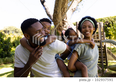Cheerful african american parents piggybacking son and daughter while standing in playground 102937591
