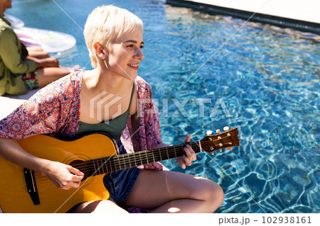 Happy caucasian woman having pool party, playing guitar and smiling in garden 102938161
