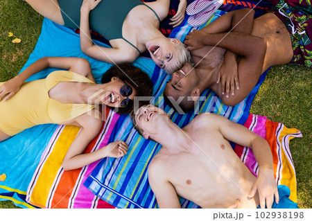Happy diverse group of friends lying on towels and laughing in garden Happy diverse group of friends lying on towels and laughing in garden 102938198