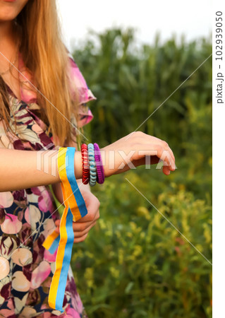 Ukraine flag. Girl wind patriotic ribbon or tape on her hand. Many bracelets. Summer outside. Vertical. Freedom, peace concept Ukraine flag. Girl wind patriotic ribbon or tape on her hand. Many bracelets. Summer outside. Vertical. Freedom, peace concept 102939050