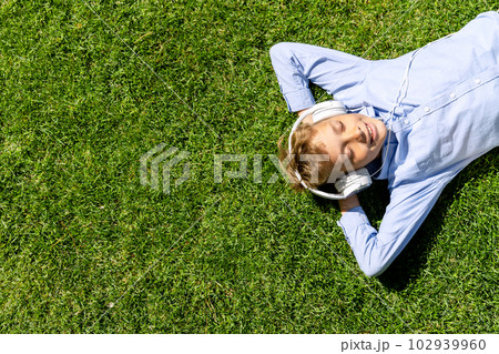 A boy relaxing on grass, listening to music A boy relaxing on grass, listening to music 102939960