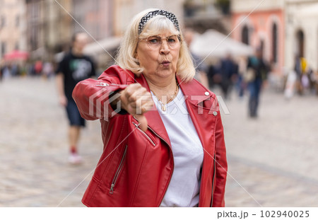 Upset senior woman showing thumbs down sign, disapproval, dissatisfied bad work, mistake in city Upset senior woman showing thumbs down sign, disapproval, dissatisfied bad work, mistake in city 102940025