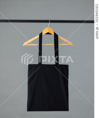 Close up of black canvas bag hanging on wooden clothes hanger with copy space on grey background Close up of black canvas bag hanging on wooden clothes hanger with copy space on grey background 102940383