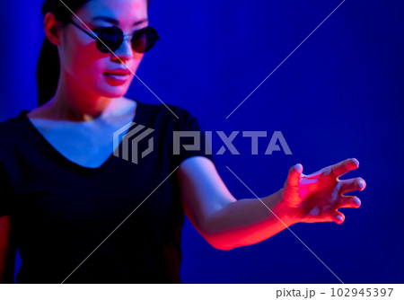 Asian woman with glasses making gesture with hand in studio with blue light with copy space Asian woman with glasses making gesture with hand in studio with blue light with copy space 102945397