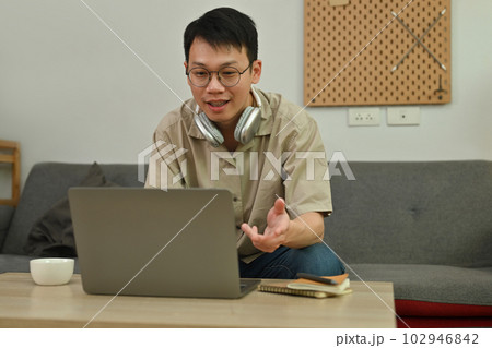 Handsome young adult man looking at laptop, talking on video call with coworkers in online briefing from home Handsome young adult man looking at laptop, talking on video call with coworkers in online briefing from home 102946842