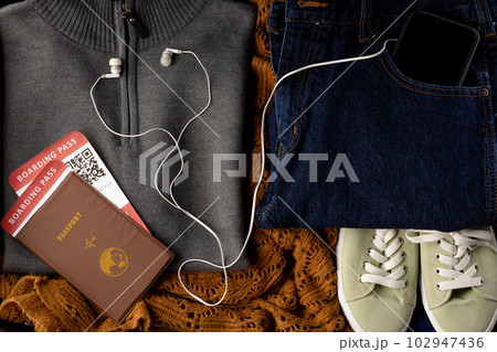 Close up of gray jumper, jeans, beige shoes, passport, tickets, smartphone and earphones Close up of gray jumper, jeans, beige shoes, passport, tickets, smartphone and earphones 102947436