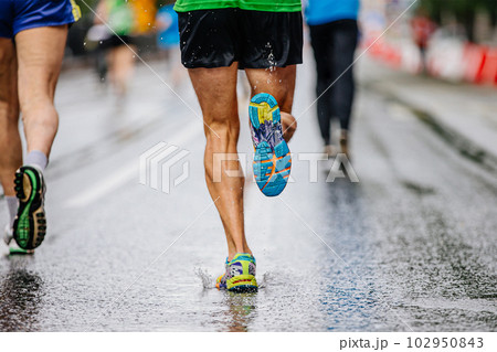 legs male runner athlete run marathon race on wet asphalt, water drops on sole running shoes legs male runner athlete run marathon race on wet asphalt, water drops on sole running shoes 102950843
