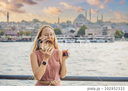 Woman in Istanbul having breakfast with Simit and a glass of Turkish tea. Glass of Turkish tea and bagel Simit against golden horn bay in Istanbul, Turkey. Turkiye Woman in Istanbul having breakfast with Simit and a glass of Turkish tea. Glass of Turkish tea and bagel Simit against golden horn bay in Istanbul, Turkey. Turkiye 102952332
