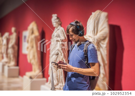 Portrait of contemporary man looking at sculptures and listening to audio guide at museum exhibition 102952354