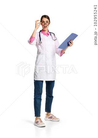 Portrait of young woman, doctor, nurse in white lab coat with stethoscope and medical papers standing with shocked face on white background 102955241