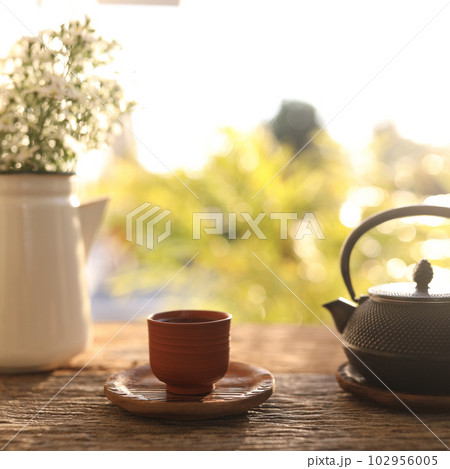Tea cup and black metal tea pot and flowers on wooden table 102956005