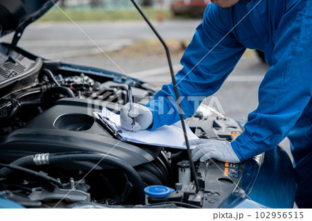 Skilled Asian mechanic in blue shirt writing repair notes on a paper, while working on a car in an auto repair shop. Close-up shot of hand. Skilled Asian mechanic in blue shirt writing repair notes on a paper, while working on a car in an auto repair shop. Close-up shot of hand. 102956515