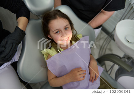 Adorable little child girl 5 years old, smiling a toothy smile looking at camera, sitting at dentist chair while visiting dental clinic for regular check-up. Pediatric dentistry. Dental oral and care 102956841
