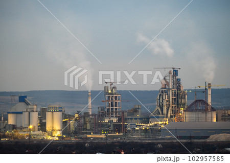 Aerial view of cement factory with high concrete plant structure and tower cranes at industrial production area at night. Manufacture and global industry concept 102957585