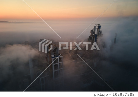 Aerial view of cement factory with high concrete plant structure and tower crane at industrial manufacturing site on foggy evening. Production and global industry concept. Aerial view of cement factory with high concrete plant structure and tower crane at industrial manufacturing site on foggy evening. Production and global industry concept. 102957588