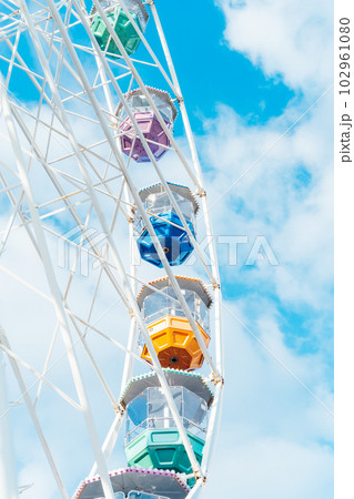Bottom view of Ferris wheel part with multicolor cabins on the background of blue sky with clouds. Vertical card. Selective focus, copy space. Bottom view of Ferris wheel part with multicolor cabins on the background of blue sky with clouds. Vertical card. Selective focus, copy space. 102961080