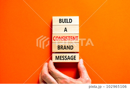 Consistent brand message symbol. Concept words build a consistent brand message on wooden blocks. Businessman hand. Beautiful orange background. Business consistent brand message concept. Copy space. Consistent brand message symbol. Concept words build a consistent brand message on wooden blocks. Businessman hand. Beautiful orange background. Business consistent brand message concept. Copy space. 102965106
