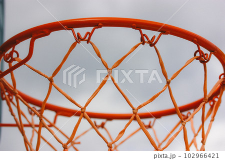 Basketball hoop on backyard against blue sky. Sports recreation and healthy living in nature. Orange red rope net on a street. Equipment on a playground. Training tools on stadium. Play outdoors. Basketball hoop on backyard against blue sky. Sports recreation and healthy living in nature. Orange red rope net on a street. Equipment on a playground. Training tools on stadium. Play outdoors. 102966421