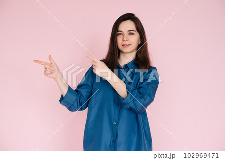Cheerful Woman Pointing with Fingers at Empty Space, Conveying Information: Vibrant Photo on Pink Cheerful Woman Pointing with Fingers at Empty Space, Conveying Information: Vibrant Photo on Pink 102969471