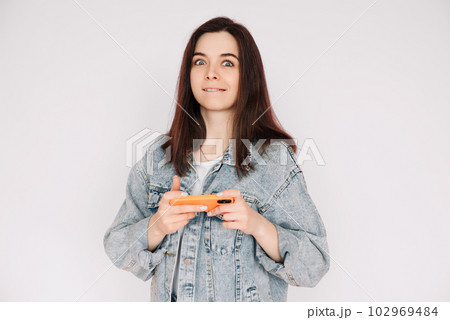 Portrait of a young woman in a casual denim jacket with a smartphone playing a game, isolated 102969484