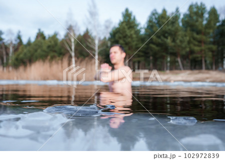 Man going ice swimming into a frozen lake during winter. Man standing between the ice pieces and meditating. 102972839