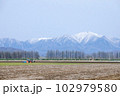 日高山脈を背景にトラクターが走る十勝平野 102979580