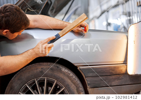 A car service worker knocks with a hammer. Removing dents on the car. PDR technology. Car body repair without painting. 102981412