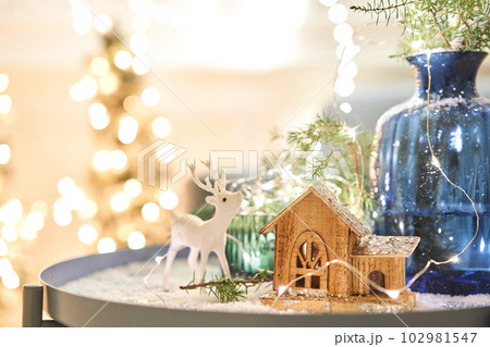 Decorated table in the Christmas interior. Christmas tree. Close-up a small house, Cones, garland, and other Christmas tree toys. light from the garlands 102981547