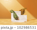 Front view of smooth yellow wall background with light in the center. Geometric platforms with marble material arranged with palm leaves. Space for advertising cosmetics product.  102986531