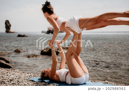 Woman sea yoga. Two Happy women meditating in yoga pose on the beach, ocean and rock mountains. Motivation and inspirational fit and exercising. Healthy lifestyle outdoors in nature, fitness concept. 102986561