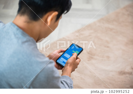 Asian older middle aged man relaxing sitting on sofa using smart mobile phone at home, Happy mature men smiling chatting with social media on smartphone in living room, holding device 102995252