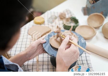 woman sculpts a figurine of a dog from clay by hands, closeup in artistic studio 102996285