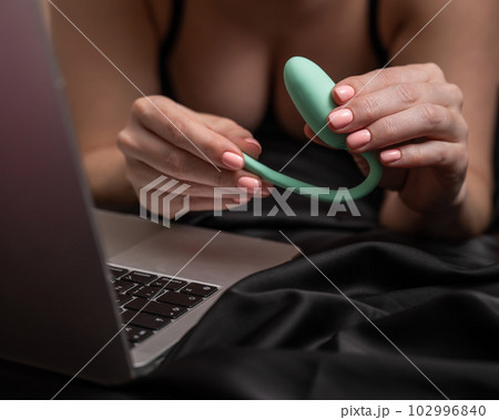 A woman lies on the bed and synchronizes the kegel machine with a laptop. A woman lies on the bed and synchronizes the kegel machine with a laptop. 102996840