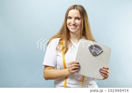 Beautiful young woman with white scales and measuring tape on blue background 102998454