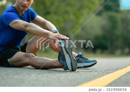 Shot of active sportsman in fitness clothes stretching leg, preparing for morning workout in the public park 102998656