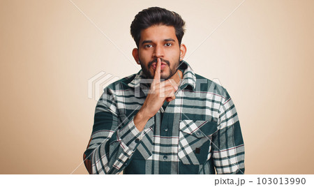 Young indian man presses finger to lips makes silence gesture sign do not tells secret, stop gossip 103013990